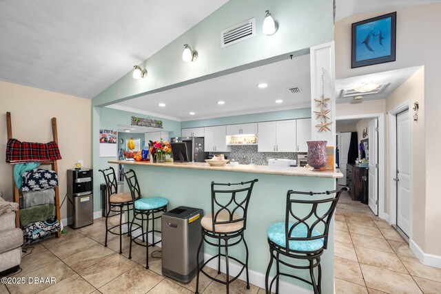 kitchen with stainless steel refrigerator, white cabinets, a kitchen bar, and kitchen peninsula