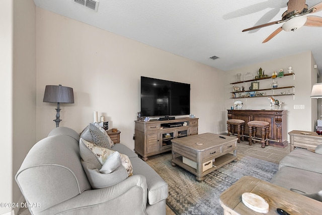 living room with light tile patterned flooring, ceiling fan, a textured ceiling, and bar area