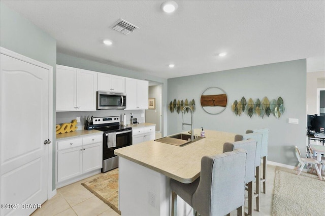 2714 Neverland Dr, New Smyrna Beach, FL 32168 - kitchen with stainless steel appliances, a kitchen bar, an island with sink, white cabinets, and light countertops