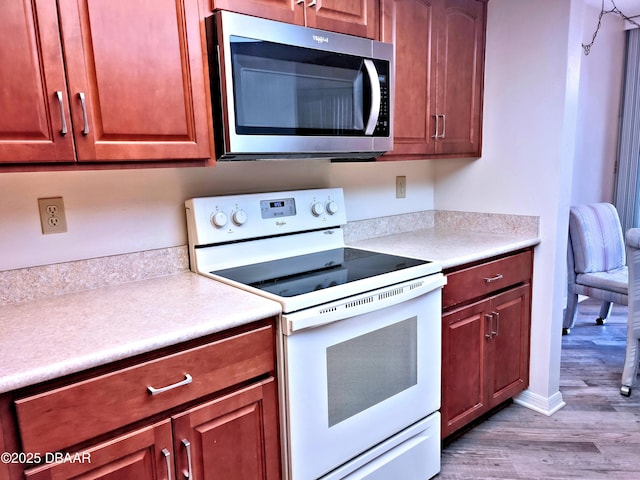 kitchen with stainless steel microwave, wood finished floors, white electric range, and light countertops