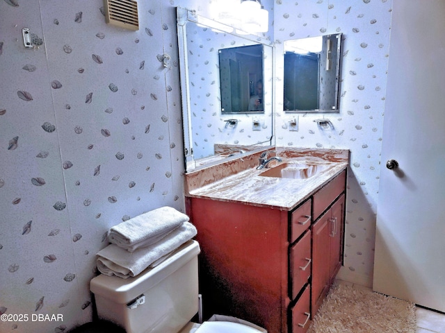 bathroom featuring toilet, vanity, and wallpapered walls