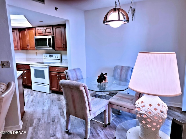 kitchen featuring stainless steel microwave, decorative light fixtures, light countertops, light wood-style floors, and white range with electric stovetop