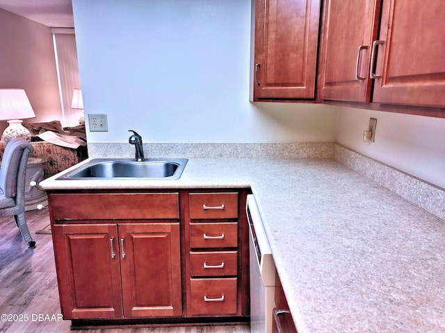 kitchen featuring light countertops, wood finished floors, dishwashing machine, and a sink