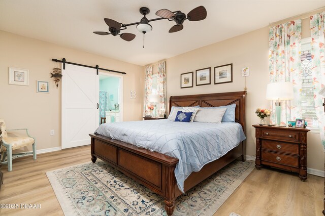 1748 Savannah Ln, Port Orange, FL 32128 - bedroom featuring a barn door, light wood-type flooring, baseboards, ensuite bathroom, and ceiling fan