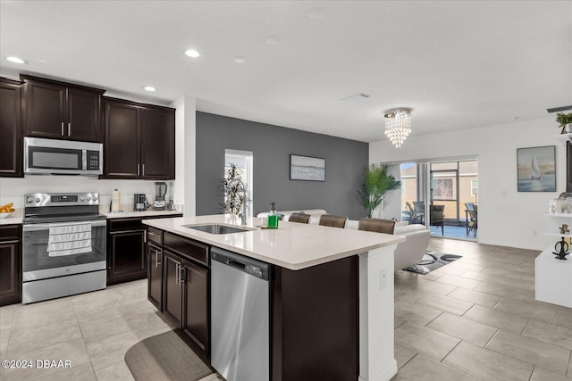 kitchen with a kitchen island with sink, sink, a notable chandelier, dark brown cabinets, and stainless steel appliances