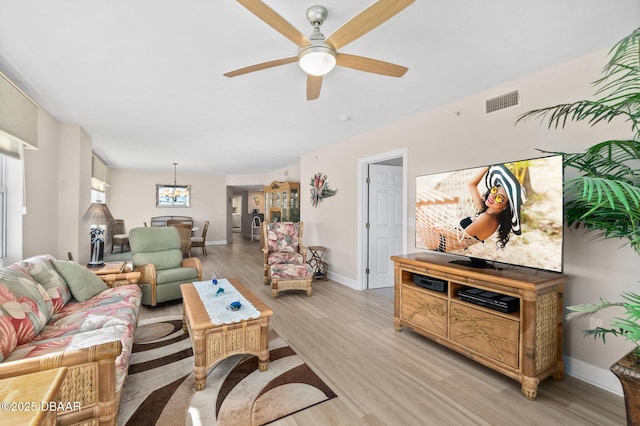 living room featuring ceiling fan with notable chandelier and light hardwood / wood-style flooring