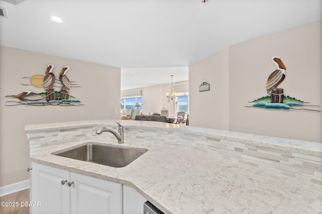 kitchen with sink, white cabinetry, an inviting chandelier, light stone counters, and decorative light fixtures