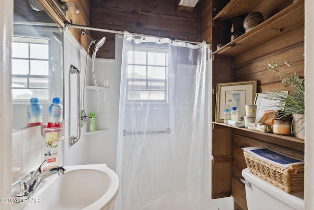 bathroom featuring a sink, a stall shower, toilet, and wooden walls