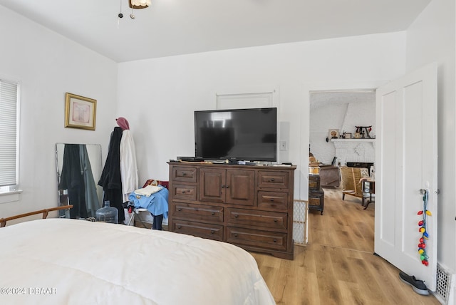 bedroom with light wood finished floors and a brick fireplace