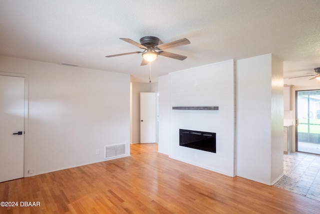 unfurnished living room with ceiling fan, a textured ceiling, and light hardwood / wood-style flooring