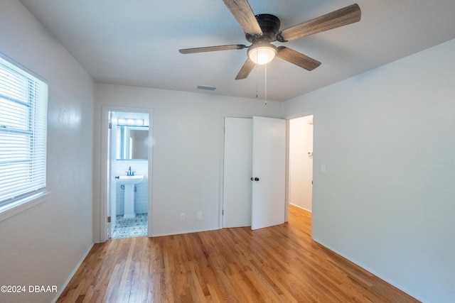 unfurnished bedroom featuring light wood-type flooring, ensuite bathroom, and ceiling fan