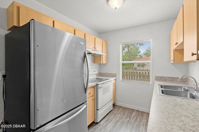 kitchen with white electric stove, freestanding refrigerator, light brown cabinets, a sink, and under cabinet range hood