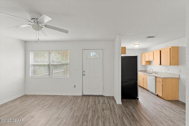 kitchen featuring light wood finished floors, freestanding refrigerator, white dishwasher, light countertops, and a sink