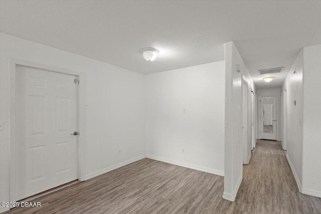 unfurnished room featuring visible vents, a textured ceiling, baseboards, and wood finished floors