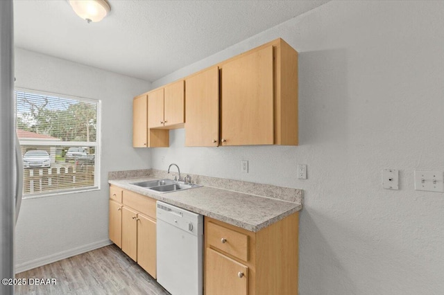 kitchen featuring white dishwasher, light brown cabinets, a sink, light wood-style floors, and light countertops