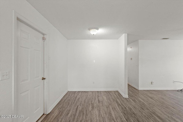 empty room with a textured ceiling, baseboards, and wood finished floors