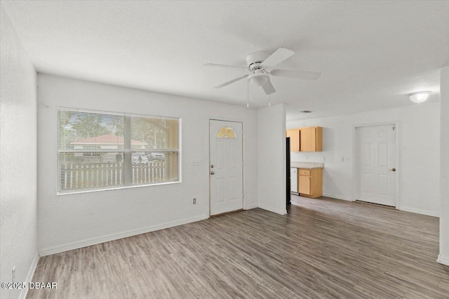 unfurnished living room with a ceiling fan, a textured ceiling, baseboards, and wood finished floors