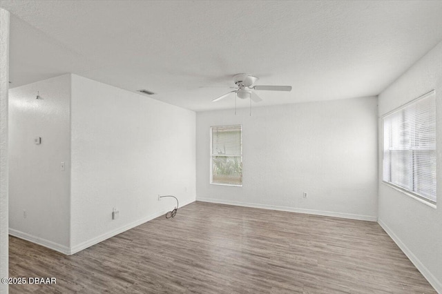 spare room featuring baseboards, visible vents, a ceiling fan, wood finished floors, and a textured ceiling