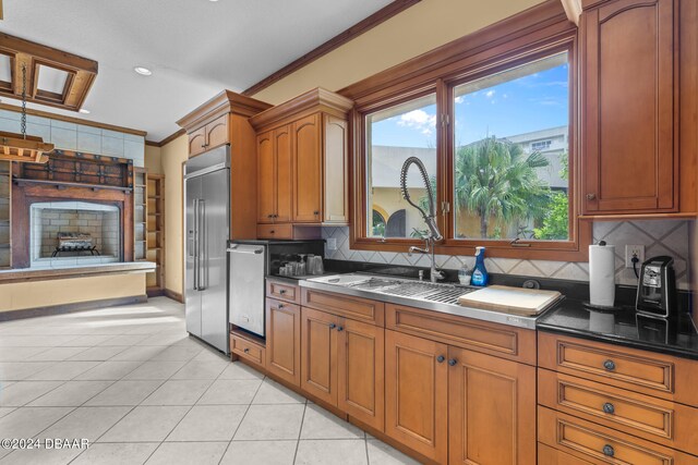 kitchen with stainless steel built in refrigerator, decorative backsplash, ornamental molding, light tile patterned flooring, and dark stone countertops