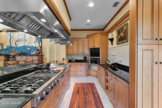 kitchen featuring stainless steel appliances, crown molding, wall chimney range hood, light tile patterned floors, and decorative backsplash