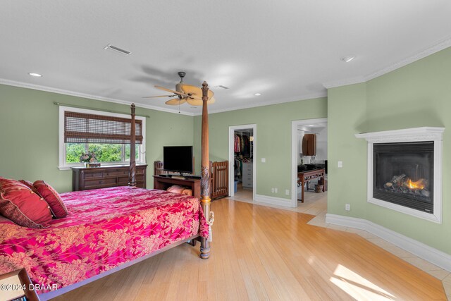 bedroom featuring ornamental molding, ceiling fan, a walk in closet, a closet, and light wood-type flooring