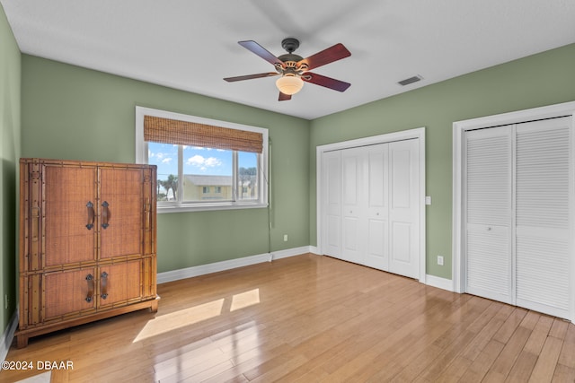 unfurnished bedroom with multiple closets, ceiling fan, and light hardwood / wood-style floors