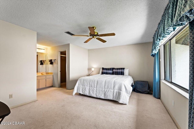 bedroom featuring a textured ceiling, light carpet, visible vents, and ensuite bathroom