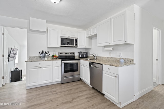 1318 San Jose Blvd, Daytona Beach, FL 32117 - kitchen featuring appliances with stainless steel finishes, white cabinets, a sink, light stone counters, and light wood finished floors