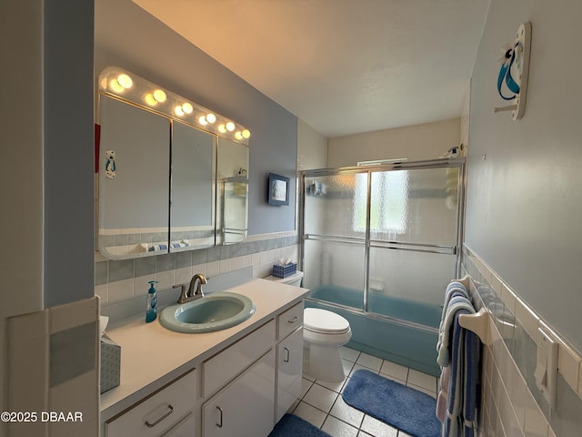 6361 Turtlemound Rd, New Smyrna Beach, FL 32169 - bathroom with tile patterned flooring, vanity, toilet, tile walls, and bath / shower combo with glass door