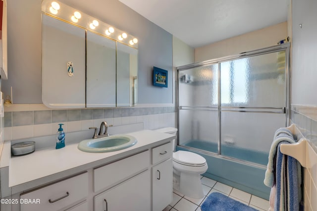 6361 Turtlemound Rd, New Smyrna Beach, FL 32169 - bathroom with vanity, toilet, tile patterned floors, tile walls, and combined bath / shower with glass door