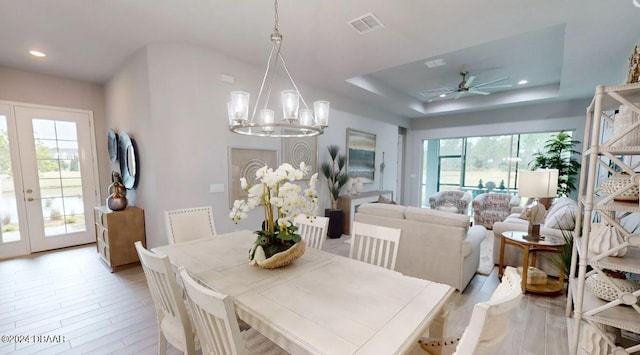 dining space with ceiling fan with notable chandelier, light hardwood / wood-style floors, a healthy amount of sunlight, and a tray ceiling