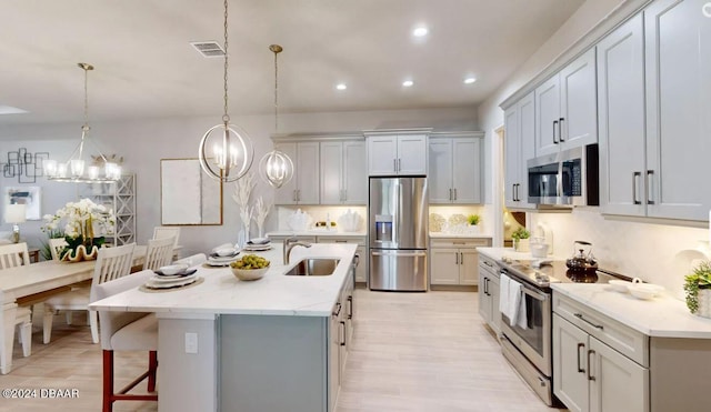 kitchen featuring stainless steel appliances, a center island with sink, sink, light wood-type flooring, and decorative light fixtures