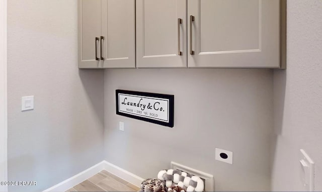 laundry area with hookup for an electric dryer, light hardwood / wood-style floors, and cabinets