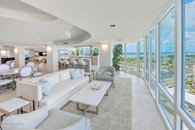 living room with a wealth of natural light, a textured ceiling, light tile patterned floors, and a wall of windows