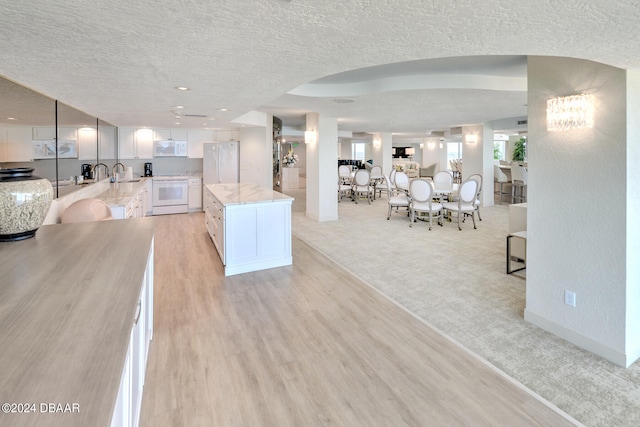 kitchen featuring white cabinetry, a textured ceiling, white appliances, and a kitchen island