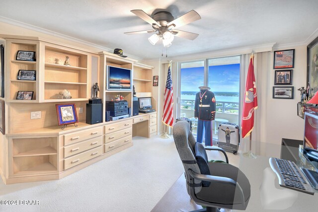 carpeted office space with built in desk, ceiling fan, and crown molding