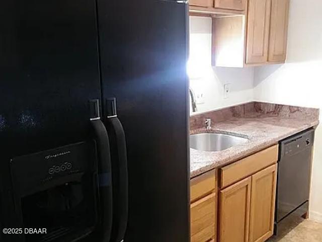 kitchen featuring light stone countertops, light brown cabinetry, sink, and black appliances