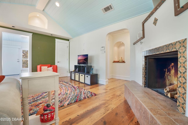 living room featuring arched walkways, lofted ceiling, visible vents, wood finished floors, and a tile fireplace