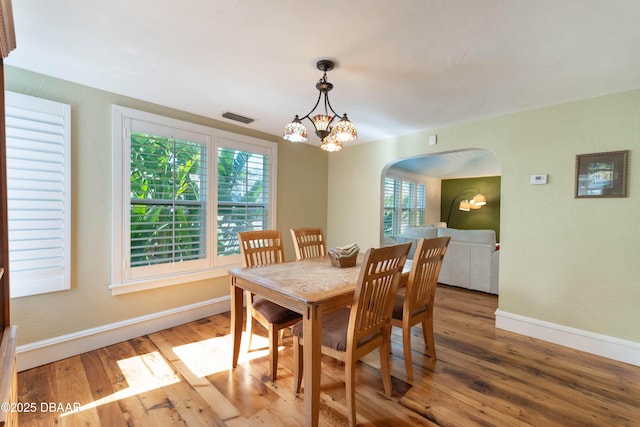 dining room with arched walkways, visible vents, an inviting chandelier, wood finished floors, and baseboards