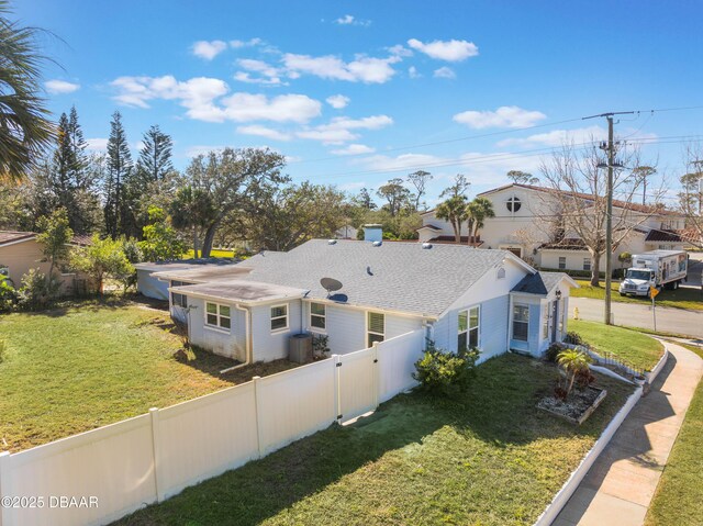 view of front facade with central air condition unit, fence, roof with shingles, a residential view, and a front yard