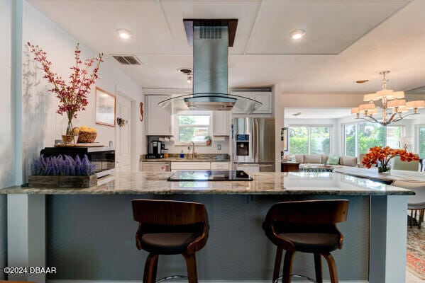 kitchen with stainless steel refrigerator with ice dispenser, a wealth of natural light, black electric stovetop, and island exhaust hood