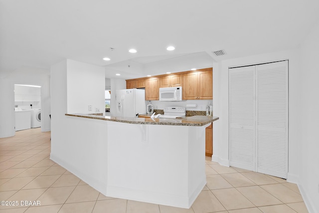 3315 S Atlantic Ave Unit 408, Daytona Beach Shores, FL 32118 - kitchen featuring white appliances, light tile patterned floors, washer / clothes dryer, dark stone counters, and a peninsula