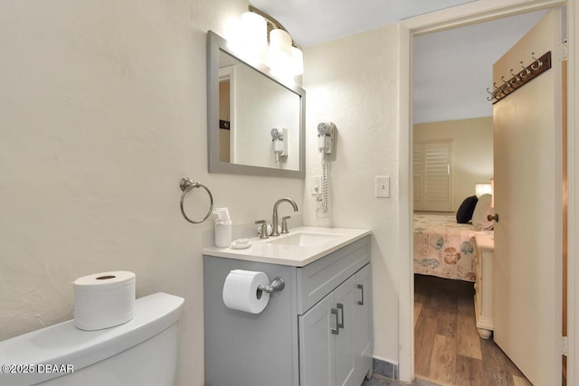 ensuite bathroom with toilet, vanity, and wood finished floors