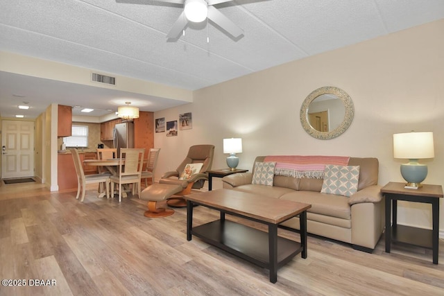 living area featuring light wood-type flooring, a ceiling fan, and a textured ceiling