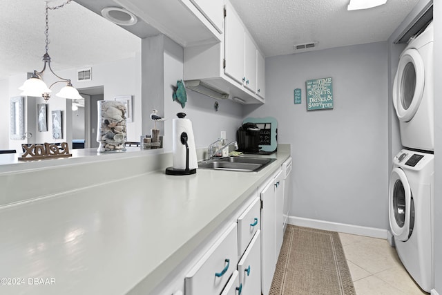 clothes washing area with stacked washer / dryer, a textured ceiling, a notable chandelier, light tile patterned floors, and sink