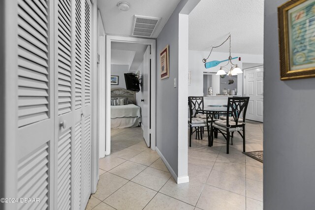 hall featuring a textured ceiling, light tile patterned floors, and a notable chandelier