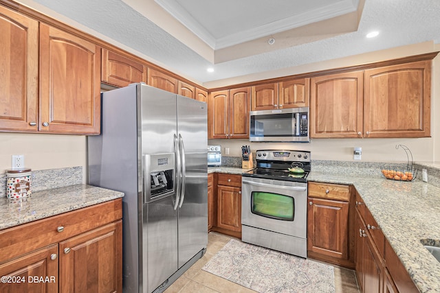 kitchen with light stone countertops, a tray ceiling, ornamental molding, and stainless steel appliances