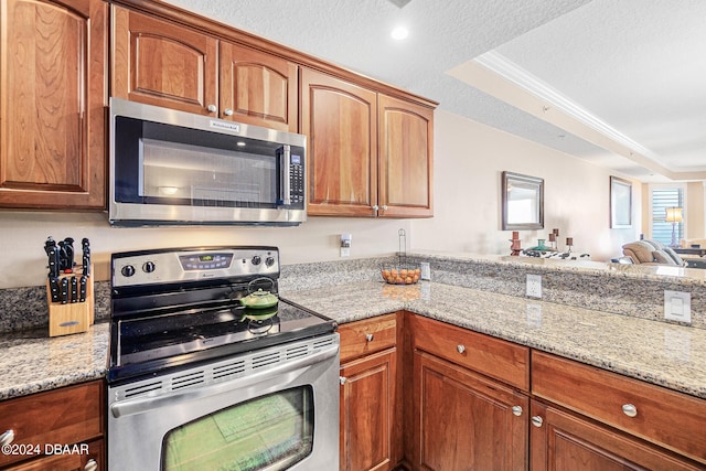 kitchen with stainless steel appliances, light stone counters, a textured ceiling, crown molding, and a raised ceiling