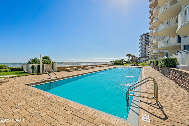 view of pool with a patio area, a water view, a beach view, and pool water feature