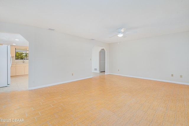 unfurnished room with visible vents, light wood-type flooring, a ceiling fan, a sink, and arched walkways